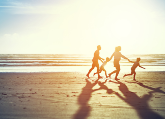 summer's not over: a family runs on a beach at sunset holding hands.