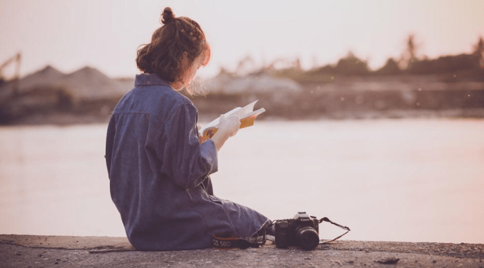 Connect with Introvert: a woman sits on a ledge over water while reading a book, with a camera next to her.