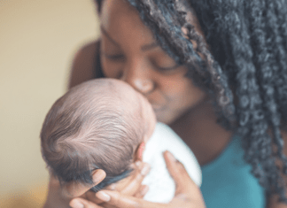 Adoption Success Story: A black woman with long hair holds and kisses the face of a white baby.