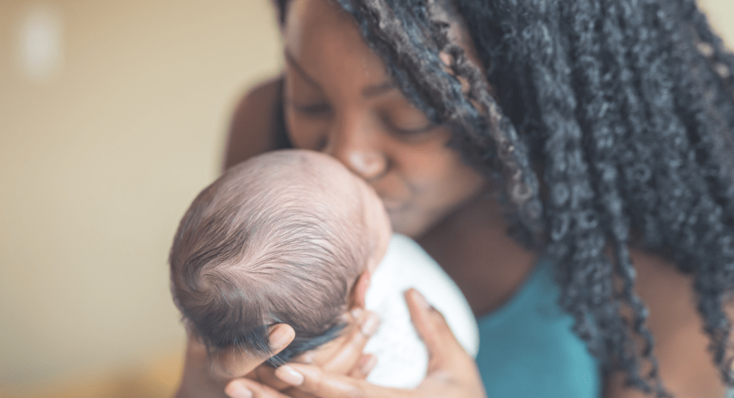 Adoption Success Story: A black woman with long hair holds and kisses the face of a white baby.