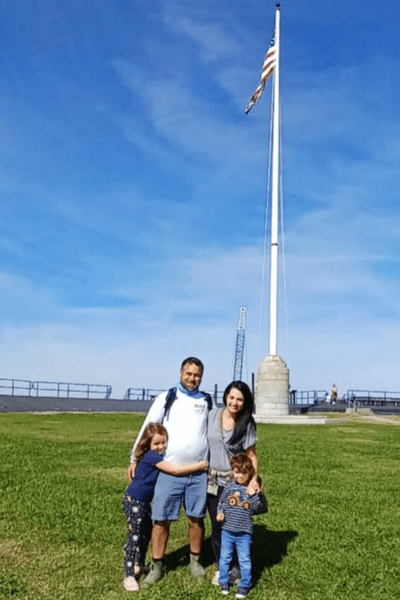 Our family of four standing atop the green field of Fort Sumter, in front of a tall flag pole with the American flag waving in the wind.