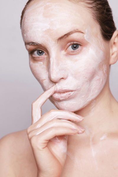 a woman poses with a white creamy face mask applied to her face.