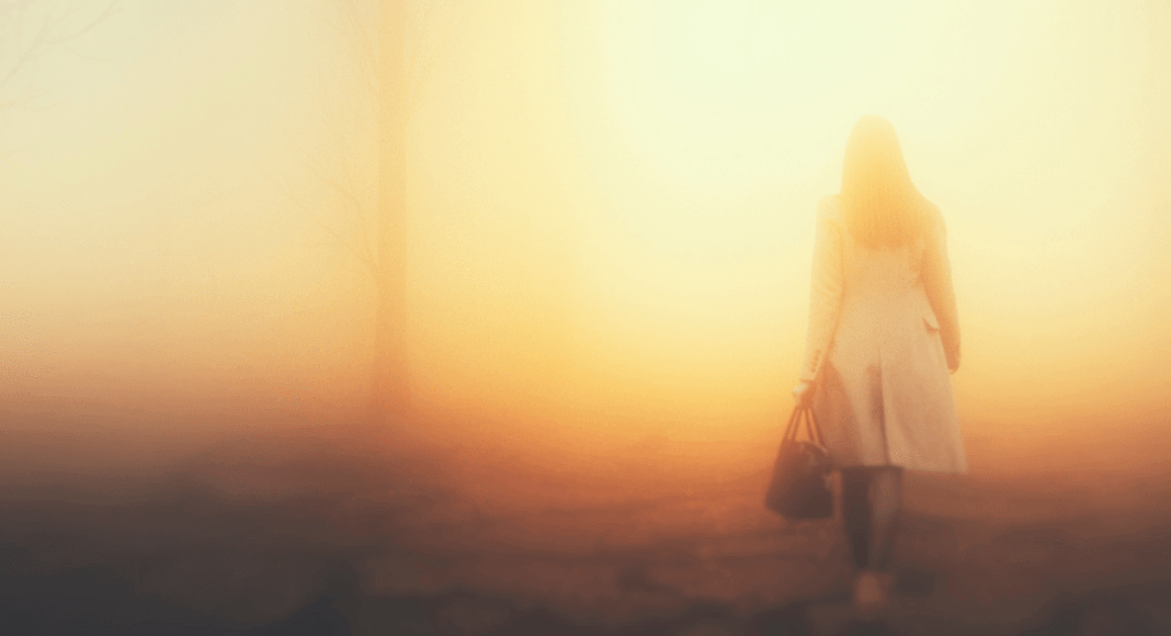 Letting go of my relationship with my mother: a woman walks away wearing a coat and holding a bag. The ground appears cracked and the background is hazy orange and yellow.