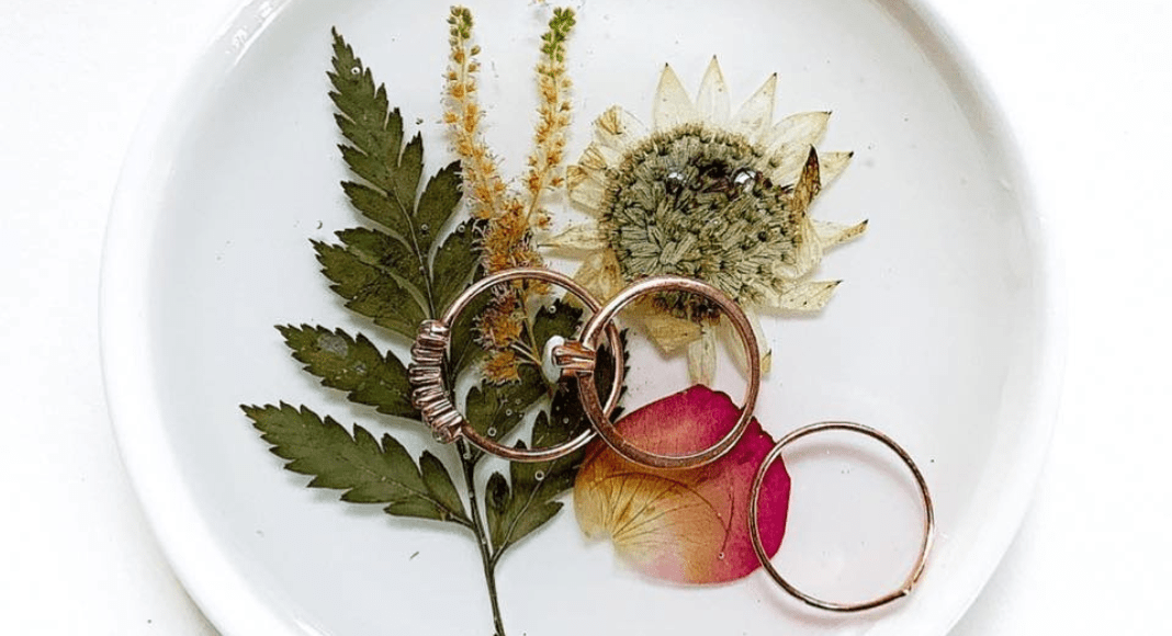 Pressed flowers and leaf sitting in a white, round dish with rings on top.