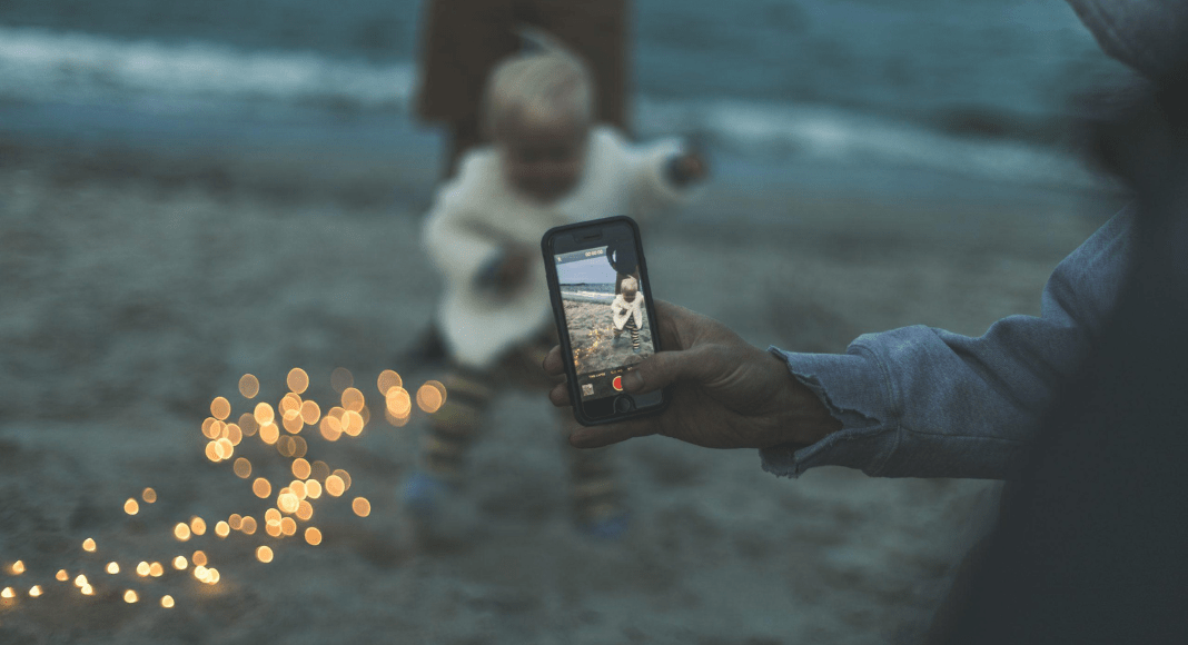 Sharenting: a parent's phone is recording their toddler on the beach.