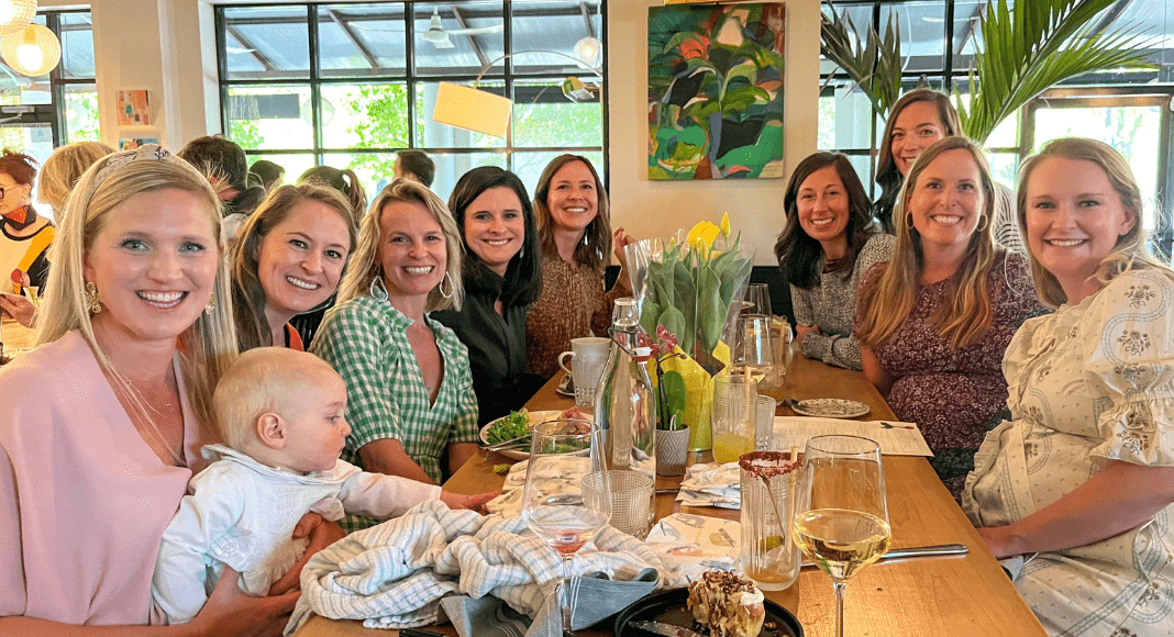 A group os women and one baby sit around a table at a restaurant. They're all smiling at the camera and have drinks in front of them.