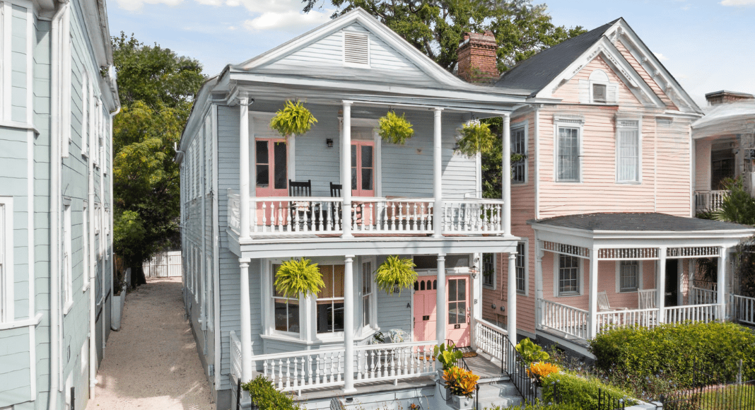 Relocating to Charleston: two older style southern homes of blue and pink with green hanging plants and shrubbery surrounding them.