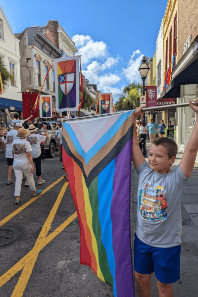 A boy holds a Pride Month flag on the side of a parade.
