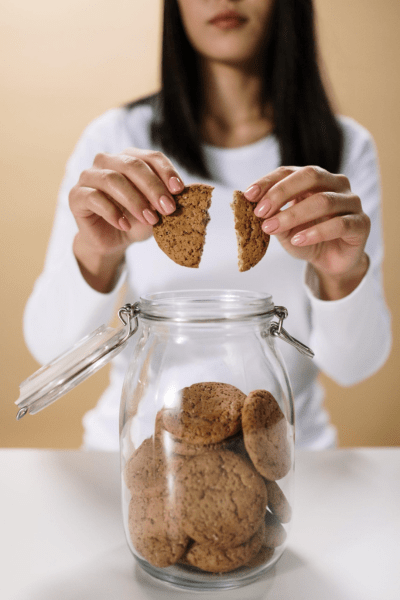 Friend fights: a woman breaks a cookie in two over a cookie jar on the counter.