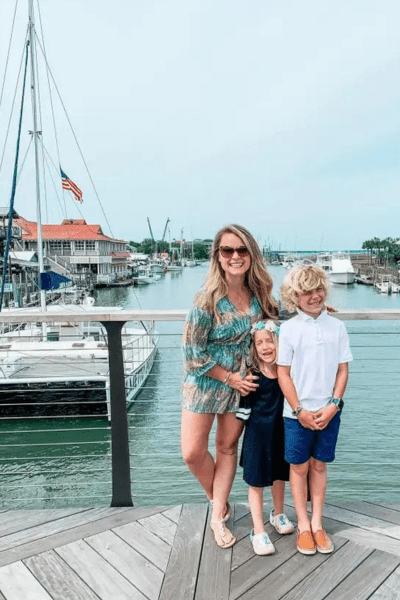 A mother and two kids stand on a dock in front of Shem Creek with boats in the background.