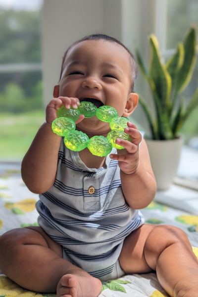 A smiley, teething baby chewing on a teething ring.