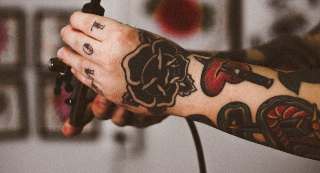 Tattoo Charleston: a tattooed arm and hand holds onto a tattoo machine.