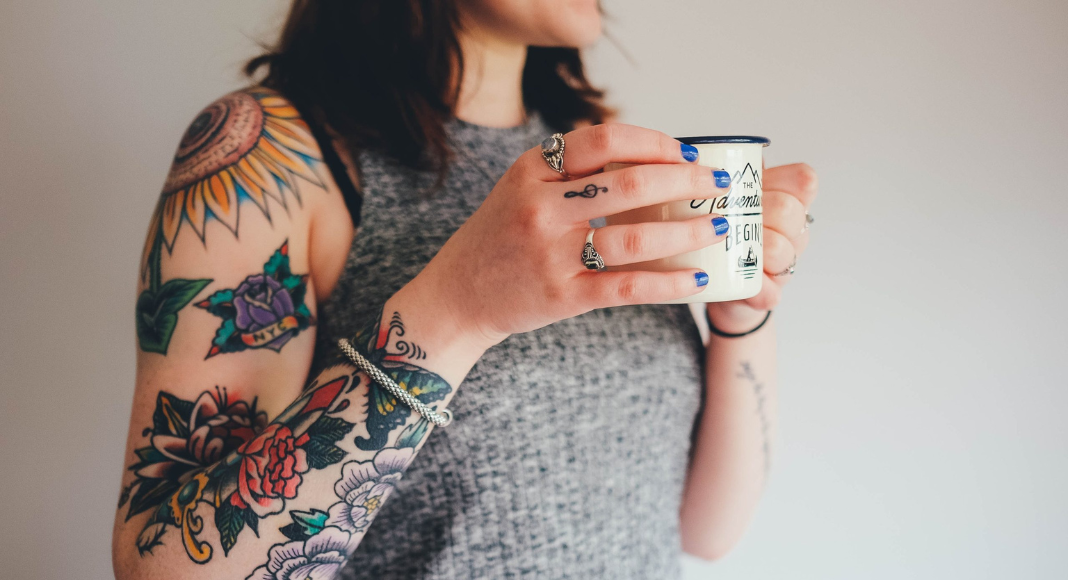 tattoo Charleston: a woman stands with a cup of coffee. Her arm is covered in floral tattoos.