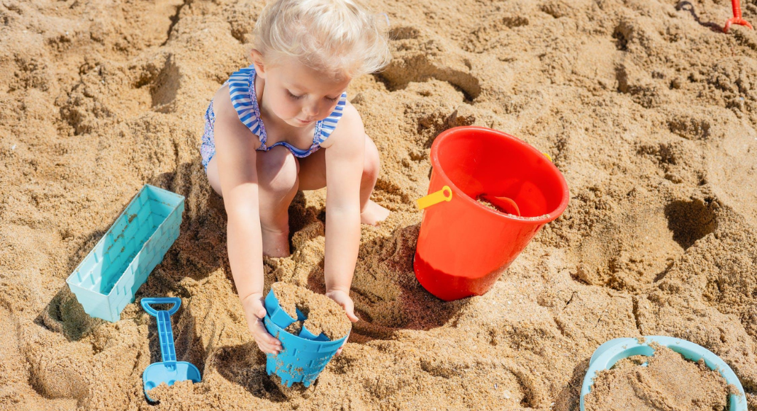 beach outing with kids: a little girl plays in sand with buckets and a shovel.