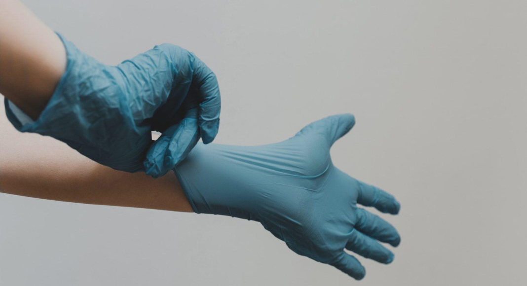 A woman's hands are shown putting on medical gloves.