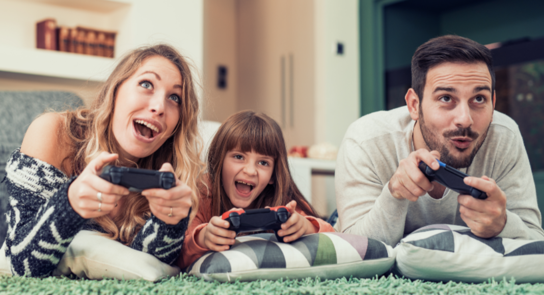 A mom and dad play a video game with their young daughter.