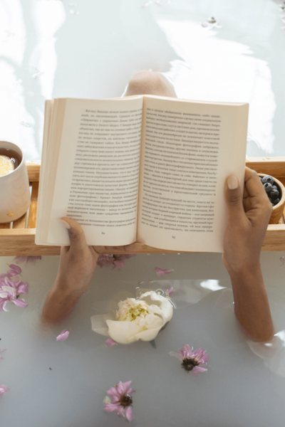 A woman rests in a bath with tea, flowers, and a book.