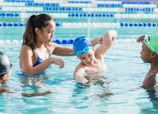 Swim Schools: a female swim instructor teaches three children in the pool.