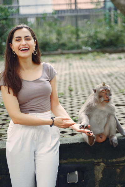 A smiling woman holds hands with a monkey.