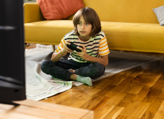 A young boy sits on the floor playing video games in front of the tv.