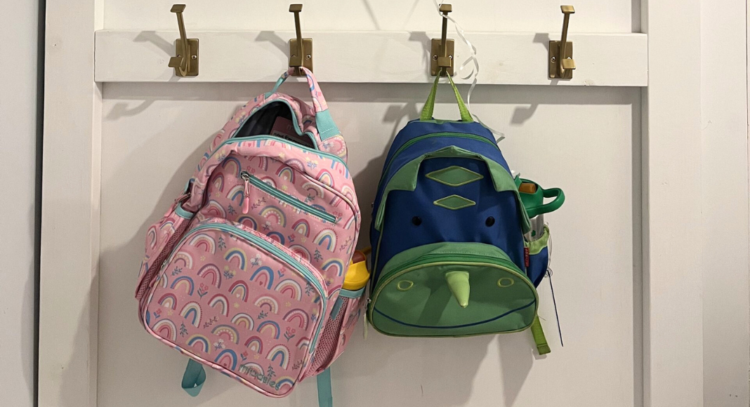 Two small backpacks hang on hooks for the school morning.