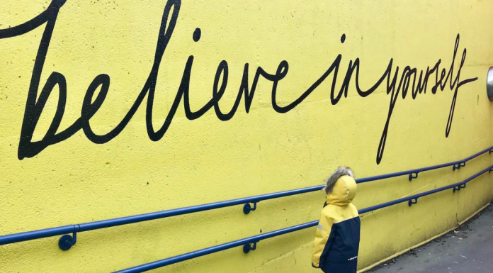Affirmations: a young child looks up at the words "believe in yourself" written in script on a wall