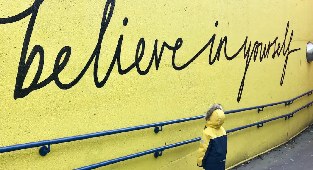 Affirmations: a young child looks up at the words "believe in yourself" written in script on a wall