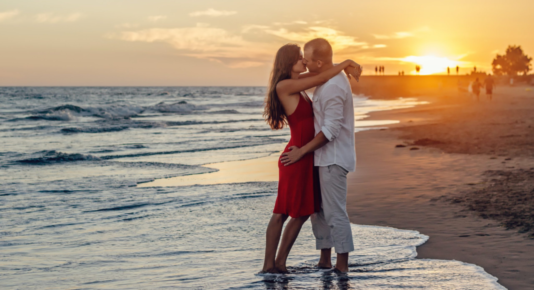 Bring sexy back: a couple kisses on the edge of the beach with a sunset behind them.