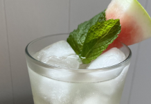 citrus water in a glass with ice, mint, and slice of watermelon on the rim.