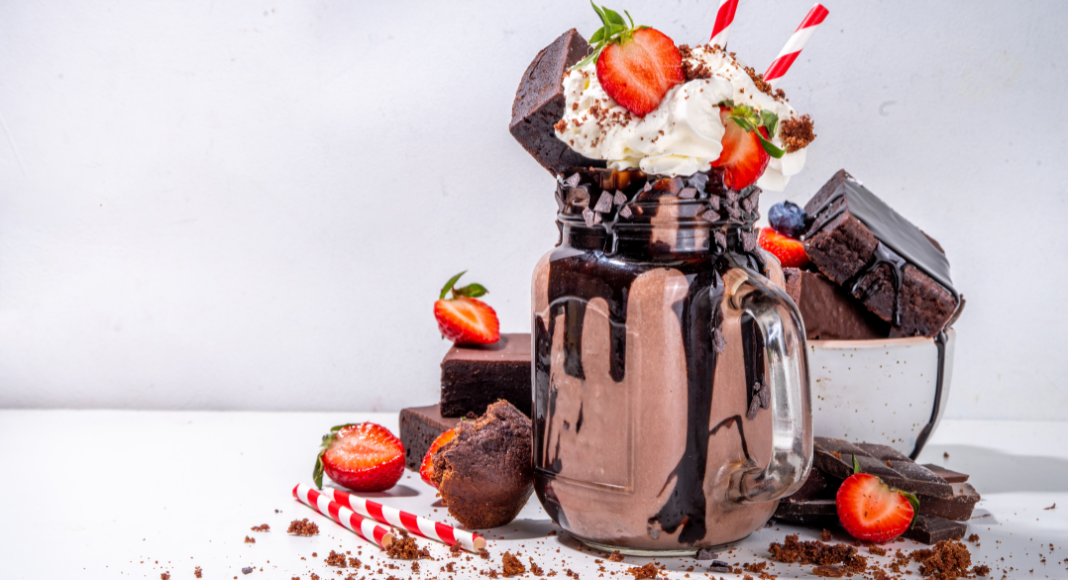 A chocolate milkshake dressed up with brownie chunks, whipped cream, and strawberries.