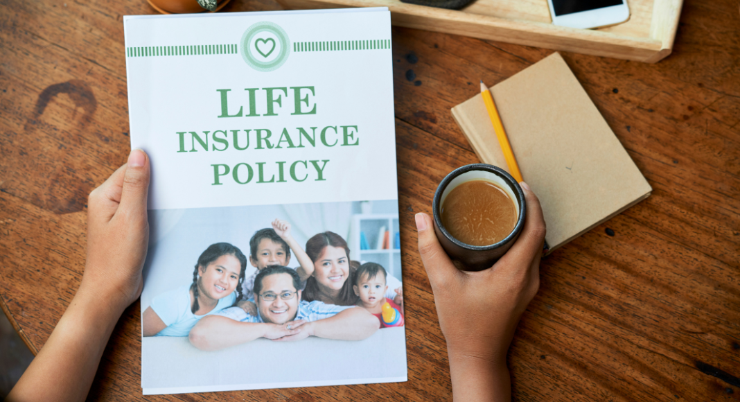 A person holds a cup of coffee and book entitled "Life insurance policy"