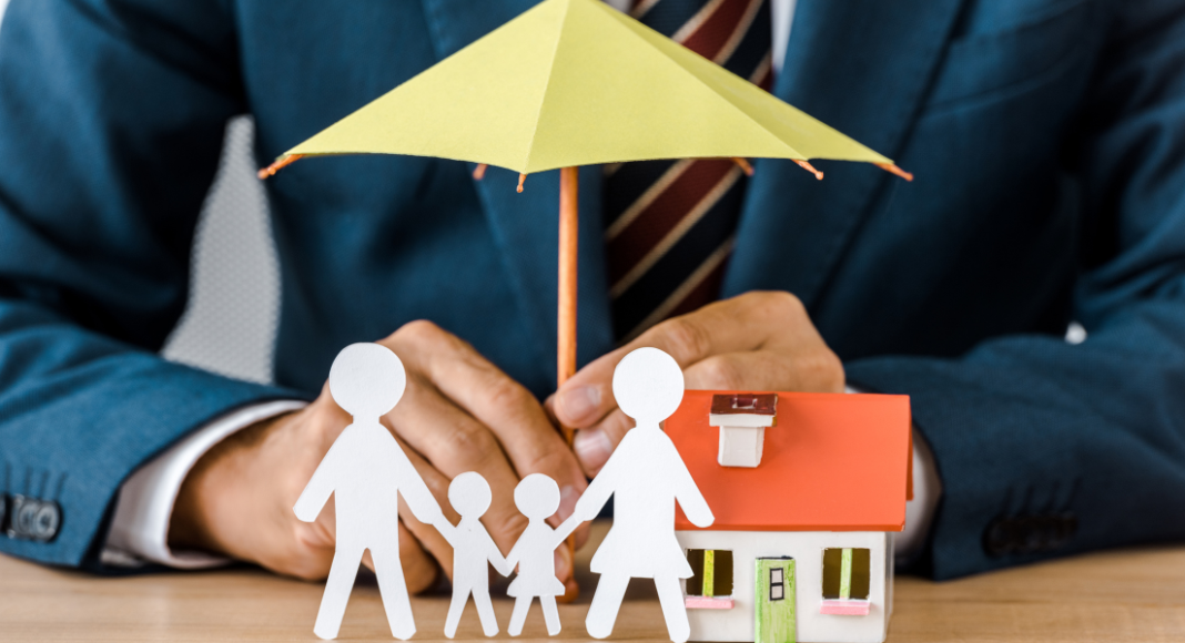 life insurance: a man in a suit holds a paper umbrella over a paper chain family and their home
