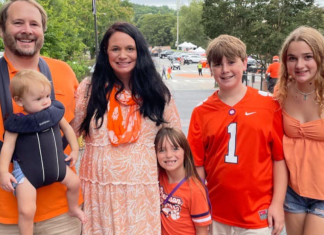 A family dressed in Clemson orange tailgating in a parking lot.