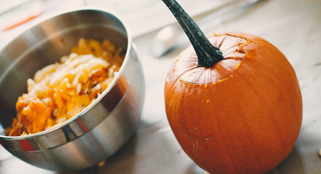 A small pumpkin sits next to a bowl full of pumpkin flesh and seeds.