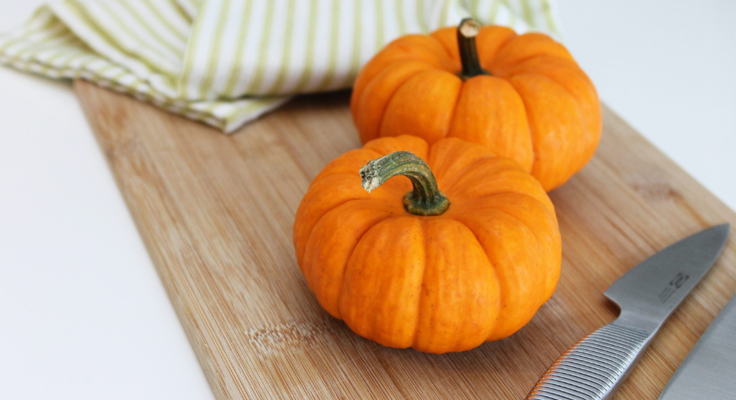 Two small pumpkins sit on a cutting board next to a towel and knife.