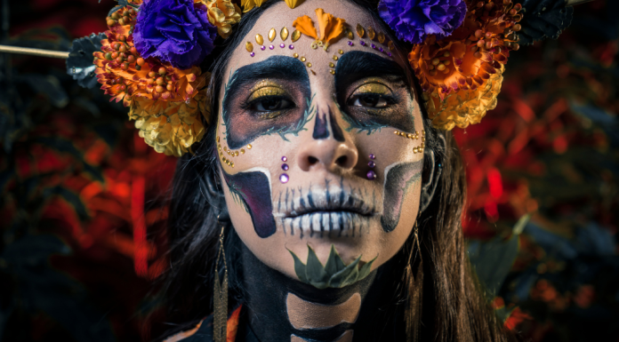 A woman dressed up with skeleton face paint, jewels, and a flower crown for Dia de los Muertos.