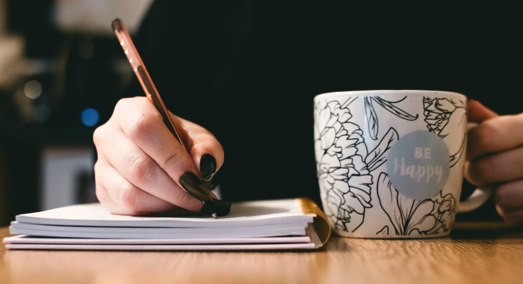 A woman with a mug, pen, and notebook for National Novel Writing Month.