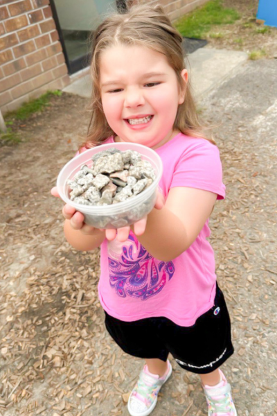 A little girl holds up a container of rocks for show and tell.