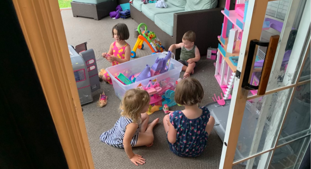 Four children play on a living room floor with toys from a bin.