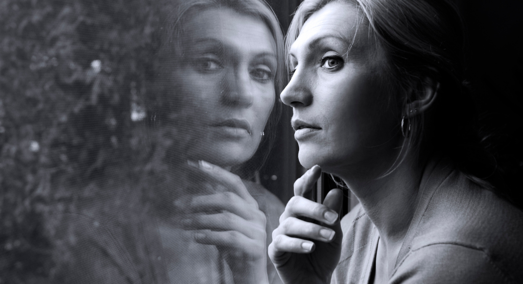 Year-end reflection: a woman looks pensively out a window. You can see her reflection in the glass.