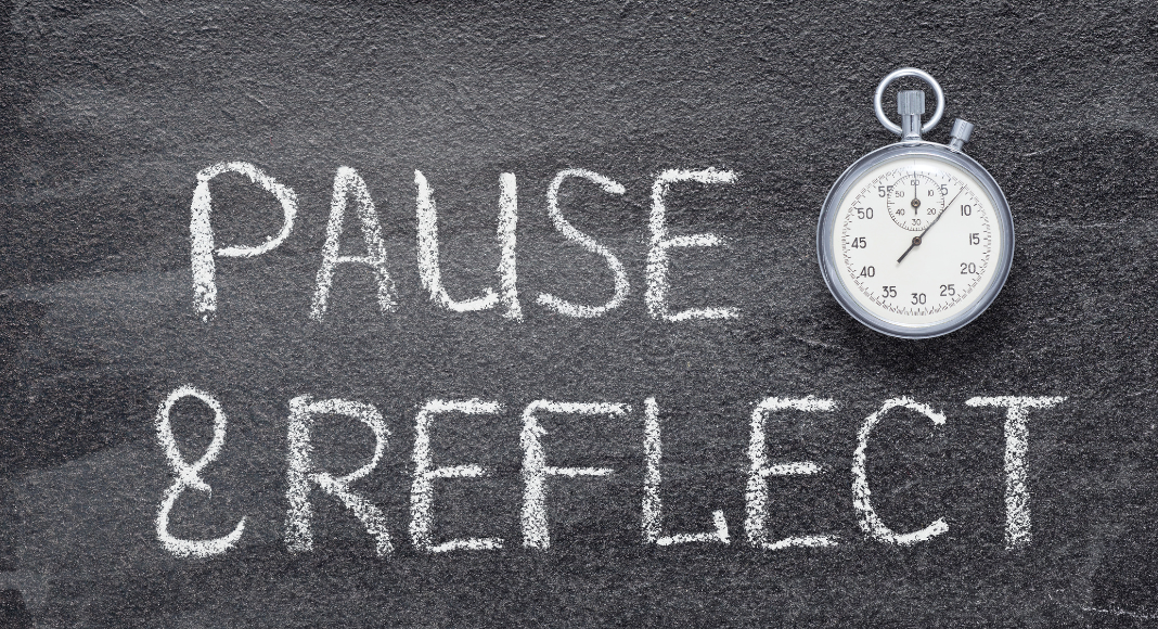 year-end reflection: The words "pause" and "reflect" on a chalkboard with a stopwatch next to it.