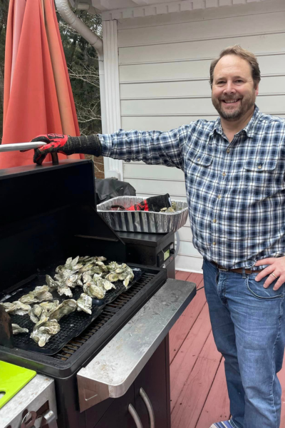Oyster roasts: a man smiles while roasting oysters on a grill