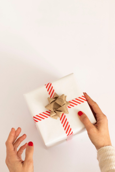 Small business gifts: A small present wrapped with white paper, ribbon, and a bow in a woman's hands.