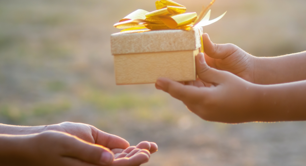 A child's hands passing a small golden present to another child.