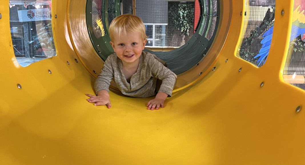 experience gifts for kids: a toddler boy crawls inside a yellow tunnel at an indoor play space