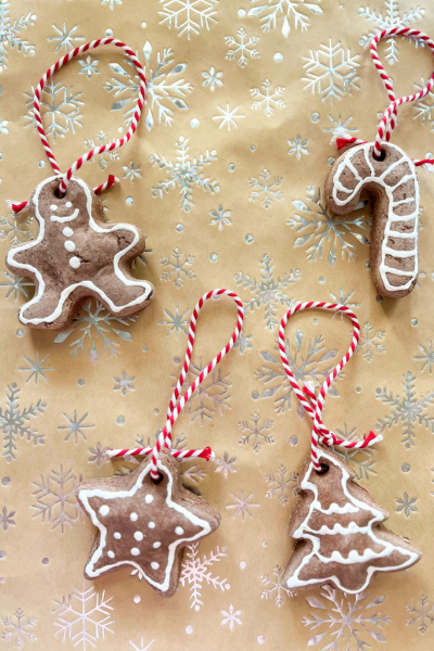 holiday crafts: 4 gingerbread ornaments in the shape of a gingerbread man, candy cane, star, and pine tree decorated with white paint and red and white striped ribbons
