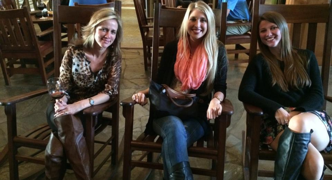 Holiday Activities in Asheville: three women sit in rocking chairs sipping on drinks.