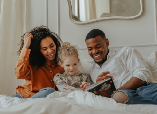 adoption and foster care resources: a family likely made through adoption read a book together on a bed.