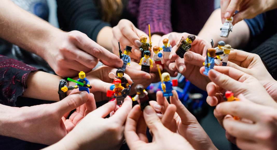 A group of people hold up LEGO Minifigures in a circle.