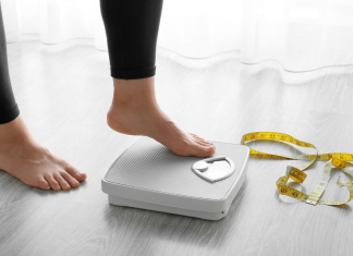 Losing weight: a woman steps onto a scale, with a measuring tape crumpled on the floor next to it.